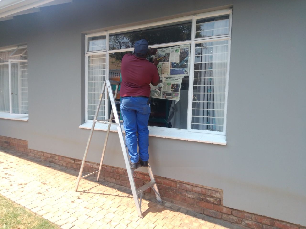 A fitter on a ladder replacing glass in a large window